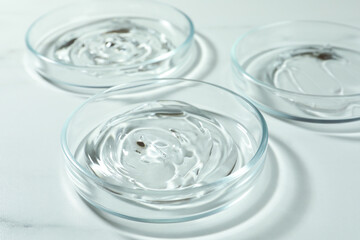 Petri dishes with liquids on white marble table, closeup