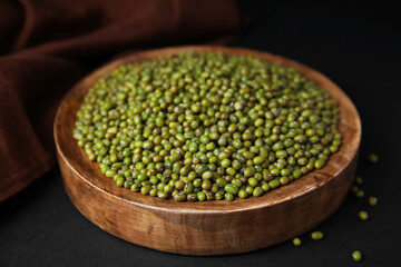 Wooden bowl with green mung beans and napkin on black background, closeup