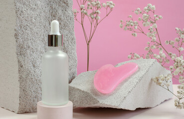 Cosmetic bottle with serum or essential oil, scraper for facial massage on the background of...