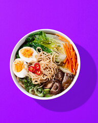 Ramen noodle soup with eggs, mushrooms, pak choi in hard light on orange