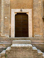 Fototapeta na wymiar Side door of Duomo di Santa Maria Assunta, Pienza Cathedral. Pienza, Tuscany, Italy. Church from 1459 with Gothic & Renaissance elements, Sienese altarpieces and Romanesque sculptures. The Pienza Duom