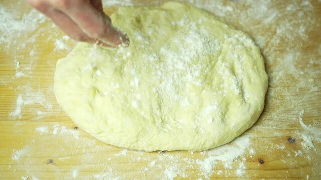 Woman's hands sprinkle dough and roll it out. Top view
