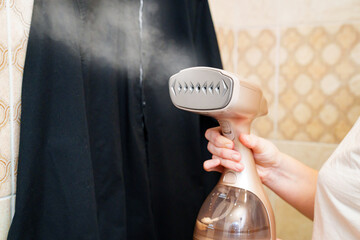 portable hand steamer for clothes in women's hands. background a black shirt 