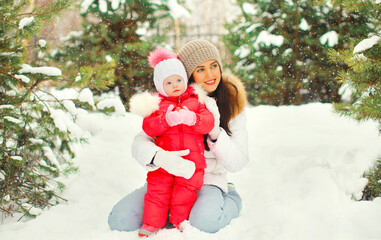 Winter portrait of happy smiling mother and little girl child outdoors on christmas tree background with snowflakes