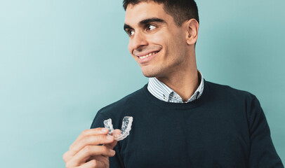 A man posing with resin splints for orthodontics. Mobile orthodontic appliance for dental correction. Placement of a bite plate in the mouth to prevent tooth death due to bruxism. - obrazy, fototapety, plakaty
