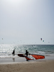 Unrecognizable wearing his wind surf. In the background unrecognizable kite surfing.