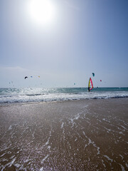 Beach on the coast of light with turquoise blue sea. Unrecognizable sailing with his windsurf. In...