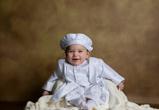 Smiling baby dressed in white clothes and brown fine art backdrop