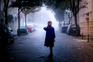 Portrait of a blond woman in an overcoat standing on a shady street.