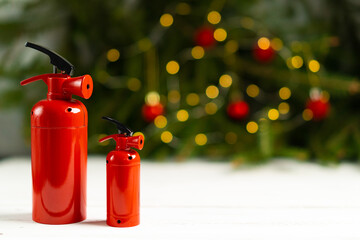 The fire extinguisher stands on a white table, against the background of a Christmas tree decorated...