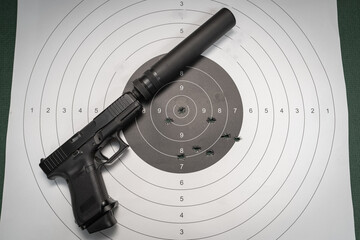 9mm pistol with silencer and target for shooting with bullet holes.