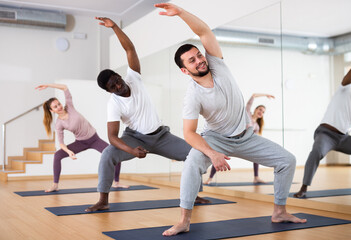 Fototapeta na wymiar Young bearded man performing stretching during group yoga class in gym. Fitness and Hatha yoga concept..