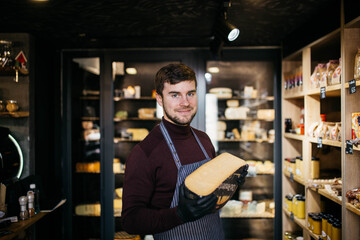 Portrait of handsome bearded man sniffing old cheese in shop.