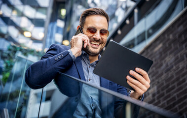 Business people. Businessman holding tablet and making a phone call in front of the corporation. Business, lifestyle concept