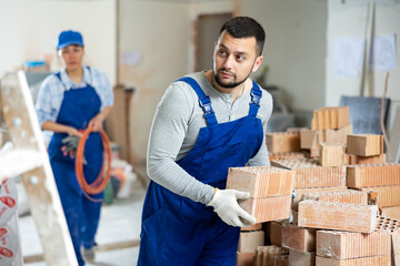 Man bricklayer carrying bricks during repair works in apartment. His female co-worker carrying...