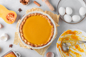 Pumpkin pie into a baking dish on a gray kitchen table surrounded by ingredients. Home cooking concept, traditional thanksgiving pumpkin pie recipe, lifestyle, top view