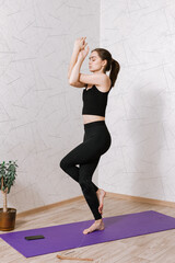 Full length of peaceful barefoot woman standing in Eagle pose with closed eyes and balancing on leg while exercising during yoga training on mat in room at home 