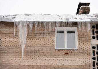 Large icicles hang from the roof of the house. Violation of the technology of thermal insulation of the roof and visor. Huge icicles are life-threatening