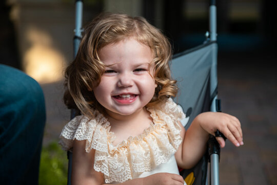Smiling little girl with brown, blonde hair and white outfit and stroller