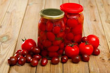 Glass jar with pickled red tomatoes and fresh tomatoes on wooden table