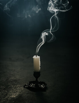 Smoke coming from a blown out candle on the floor of a dark room.