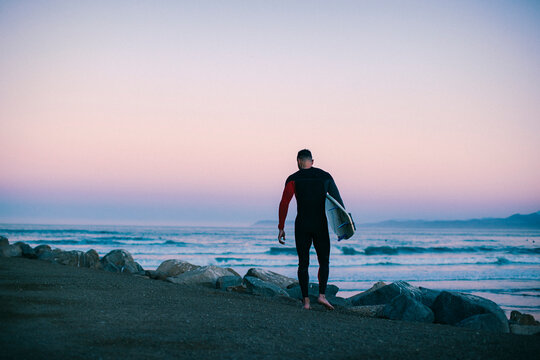 A middle aged man walks towards the beach with a surfboard.