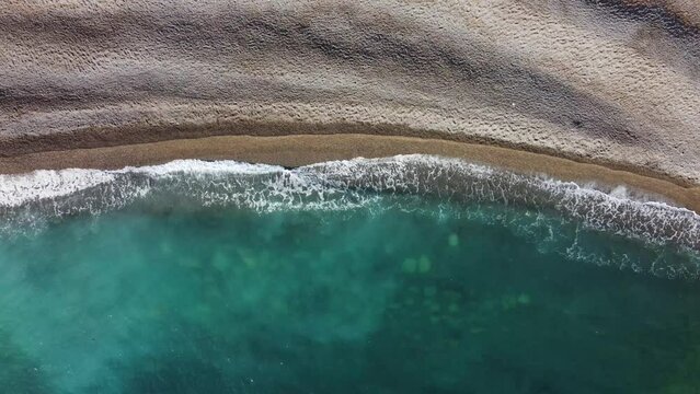 waves of turquoise sea splashing over brown beach, no people, aerial view