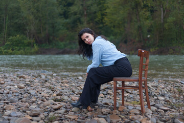 A young girl sits on a chair, on the bank of the river, foggy weather