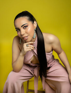 Smiling portrait of a woman in pink jumper and yellow backdrop