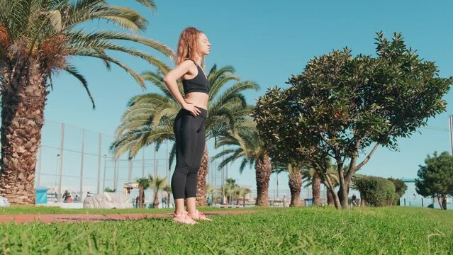 Head rotation, prevention of atrophy of cervical muscles young woman. Woman warming up the neck in standing position. Tropical park with people who take care of their health