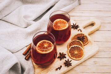 Two glasses with mulled wine on wooden cutting board with spices and orange slices, top view