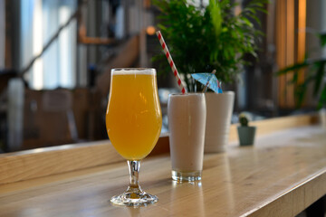 A clear glass stem beer glass filled with a pale ale and a chocolate smoothie in a tall clear glass...