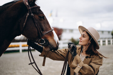 Obraz premium A young woman in a brown coat and hat near a horse.