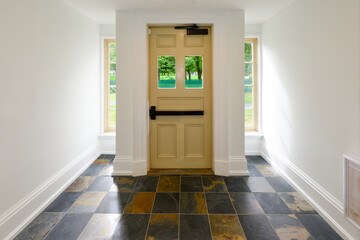 The interior of a bright and light hallway of an office building. The flooring is large black and gold color tiles. The walls are white and the metal door has two small glass windows and a push bar. 