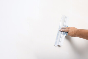 Worker plastering wall with putty knife indoors, closeup. Space for text