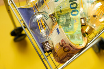 Light bulbs and euro banknotes in a supermarket trolley on a yellow background.Crisis in the energy...