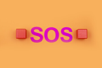 Abbreviation SOS made of paper letters and wooden cubes on orange background, flat lay