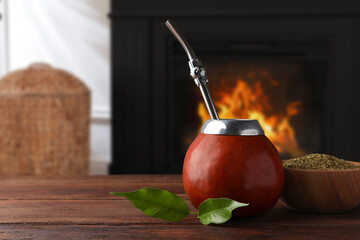 Calabash with mate tea and bombilla on wooden table near fireplace. Space for text
