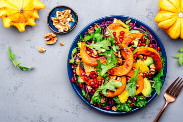 Healthy vegan eating, autumn pumpkin salad with baked honey pumpkin slices, lettuce, arugula, pomegranate seeds and walnuts. Comfort food. Top view