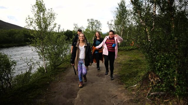 Tracking shot of a group of people walking on a beautiful trail surrounded by trees, Torne River and mountain while enjoying together