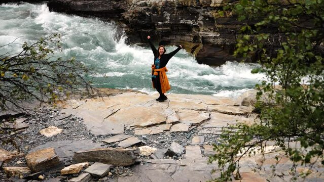 Static shot of a woman standing and cheering with open arms and her back on Torne River inside Aurora Camp Kurravaara, Sweden
