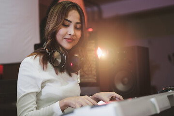 Asian producer woman in white shirt playing piano in sound studio with warm lighting background,...