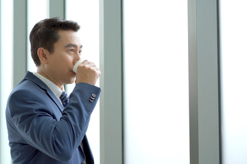 Smart and good looking Asian businessman relaxing and drinking a coffee, senior manager drinking a coffee during a coffee break in afternoon. Photograph with copyspace.
