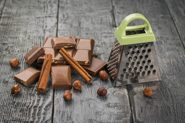 Chocolate, cinnamon, nuts and a grater on a wooden table.