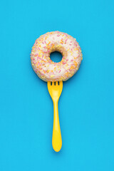 A yellow fork in a glazed donut on a blue background. The minimal concept of popular baking.