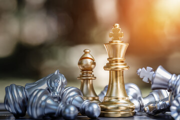 Chess king and bishop stood on chessboard surrounded by other pieces lying on their opponent's...