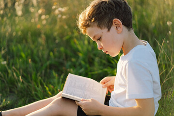 Fototapeta premium Christian boy holds bible in her hands. Reading the Holy Bible in a field during beautiful sunset. Concept for faith, spirituality and religion. Peace, hope