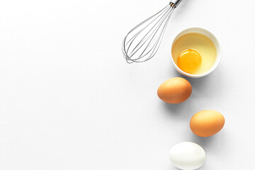 Flatlay or packshot top down view raw Eggs with a bowl of cracked egg yolk and whisk for cooking on white paper isolated background and space