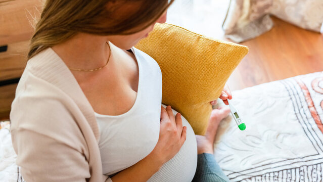 Pregnancy health temperature check. Pregnant woman holding thermometer, check fever flu temperature. Pregnancy girl sick. Concept maternity, pregnant, childbirth.