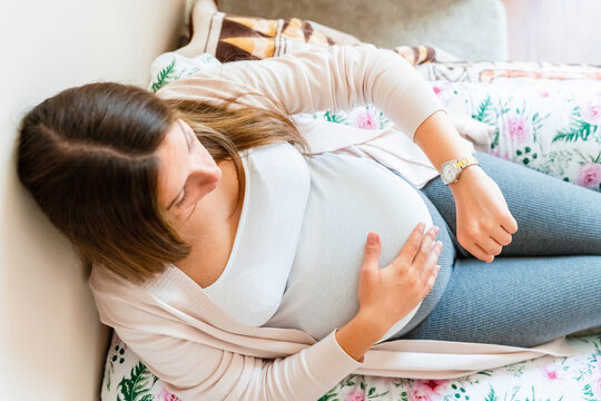 Pregnancy contractions time. Childbirth time, contractions pain. Pregnant holding baby belly, woman watching clock. Therapy, healthcare, motherhood concept.